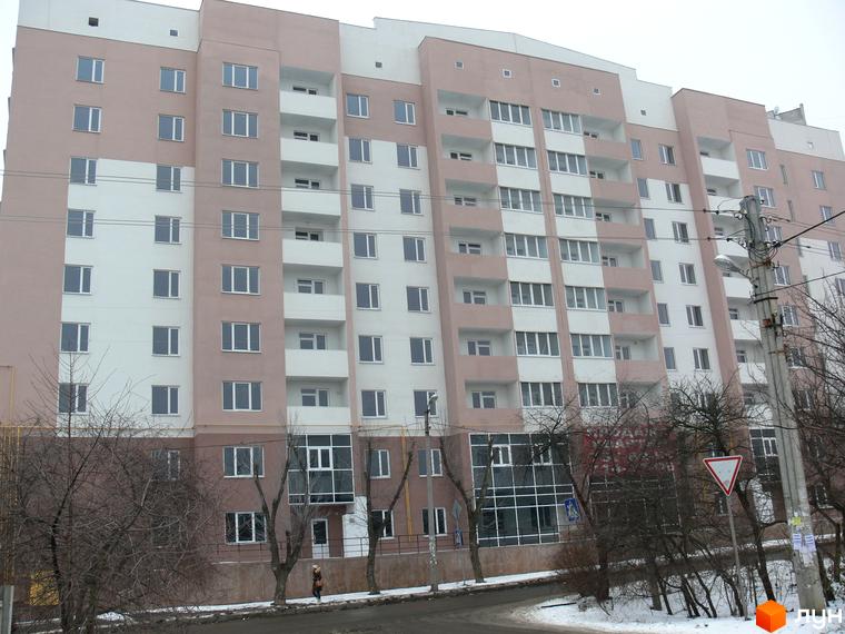 Житловий комплекс Супутник - багатоповерховий будинок з біло-рожевим фасадом та численними вікнами. Навколо будівлі видно дерева та дорогу.