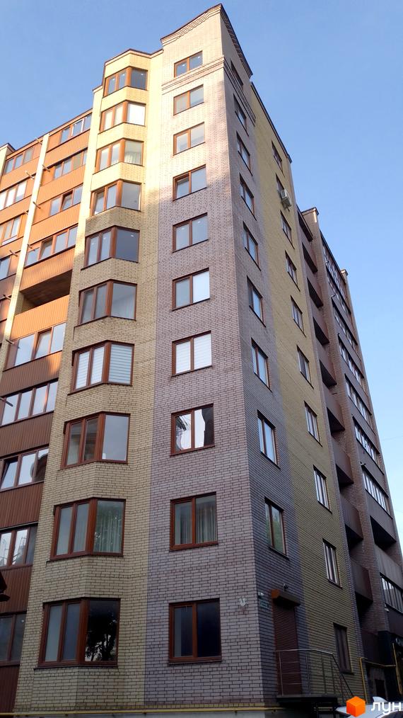 Фасад житлового комплексу на вулиці Тарнавського, 30, з цегляним оздобленням та великою кількістю вікон. Будинок має багатоповерхову структуру з балконами.