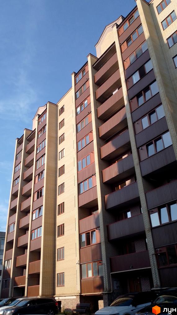 Зовнішній вигляд житлового комплексу на вул. Тарнавського, 30, з цегляним фасадом та коричневими балконами. На прибудинковій території видно припарковані автомобілі.