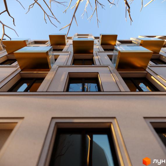 Будинок ЖК Residence Eleven з золотими балконами та великими вікнами на тлі блакитного неба та гілок дерев.