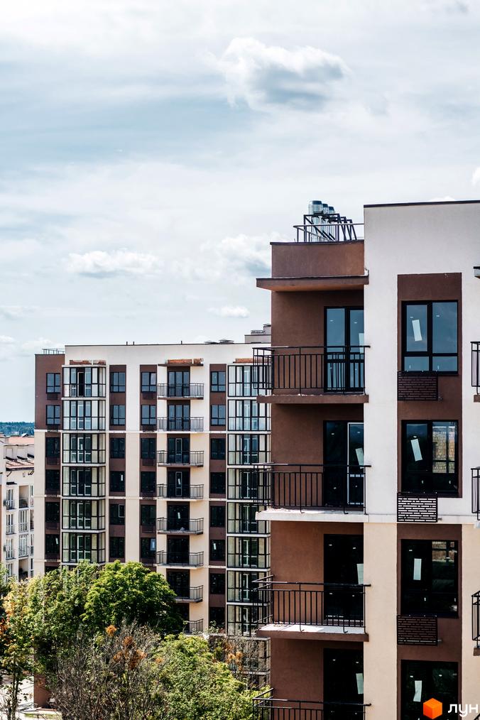 Зовнішній вигляд багатоповерхового будинку ЖК Кришталеві джерела з балконами та великими вікнами. Навколо будівлі зелені дерева.