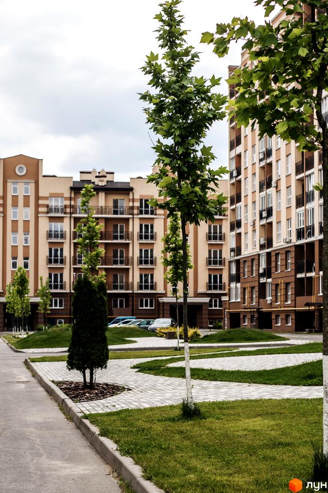Житловий комплекс Кришталеві джерела. Багатоповерхові будинки світло-бежевого кольору з коричневими елементами та балконами. Прибудинкова територія з доглянутими газонами та доріжками.
