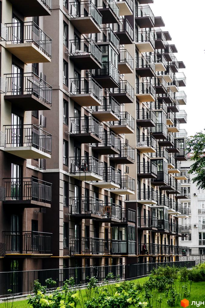 Фасад житлового комплексу Кришталеві джерела з численними балконами та вікнами. Прибудинкова територія з зеленою травою та огорожею.