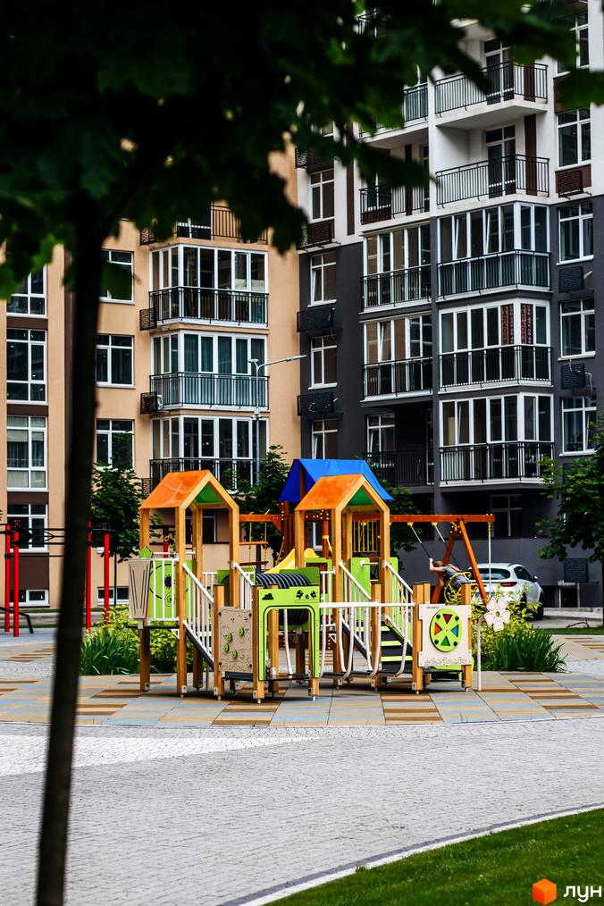 Житловий комплекс Кришталеві джерела. Сучасний дитячий майданчик біля багатоповерхових будинків з балконами та вікнами.