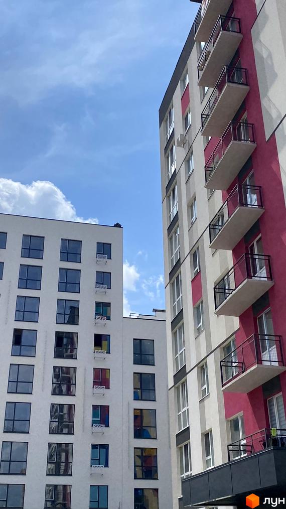 Зовнішній вигляд новобудови ЖК Синергія Color з фасадами білого та рожевого кольорів та численними вікнами. Будівельний проєкт з сучасними балконами.