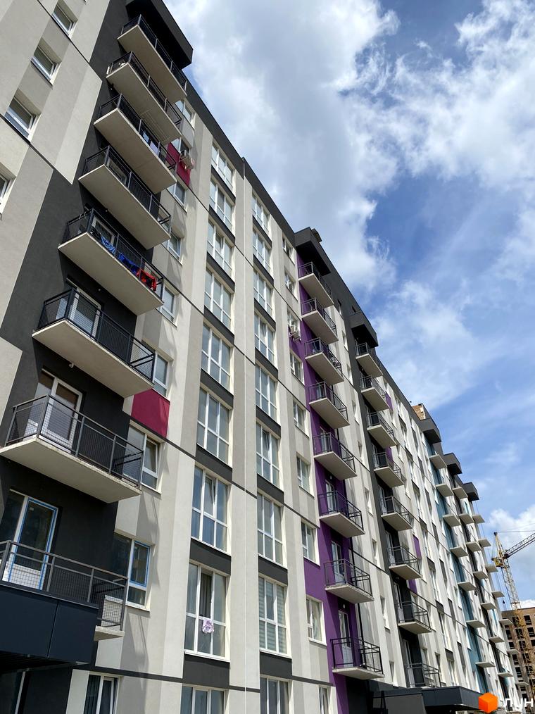 Фасад житлового комплексу Синергія Color з балконами та вікнами на тлі хмарного неба. Будівельний проєкт з яскравими кольоровими акцентами.