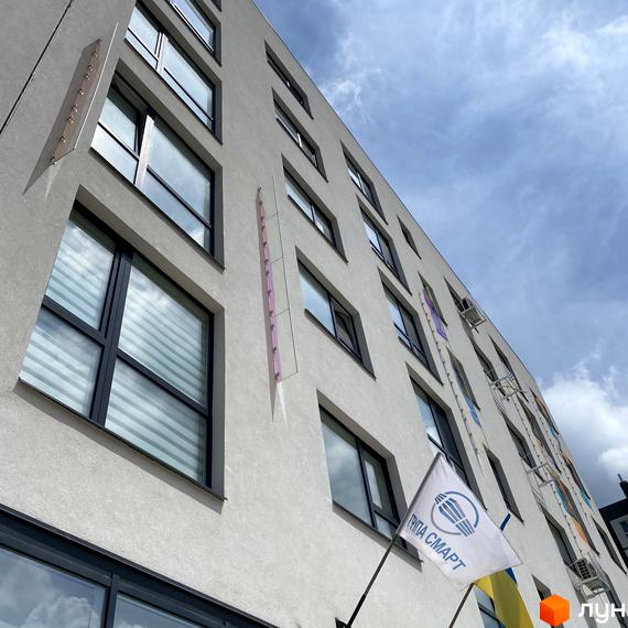 Зовнішній вигляд Житлового комплексу Синергія Glass з великими вікнами. На фасаді будівлі розміщено прапор та логотип забудовника.