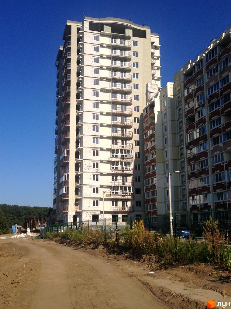 Житловий комплекс Маяк - висотна новобудова на етапі будівництва з балконами та вікнами. Навколо будівельний майданчик з дорогою та зеленню.