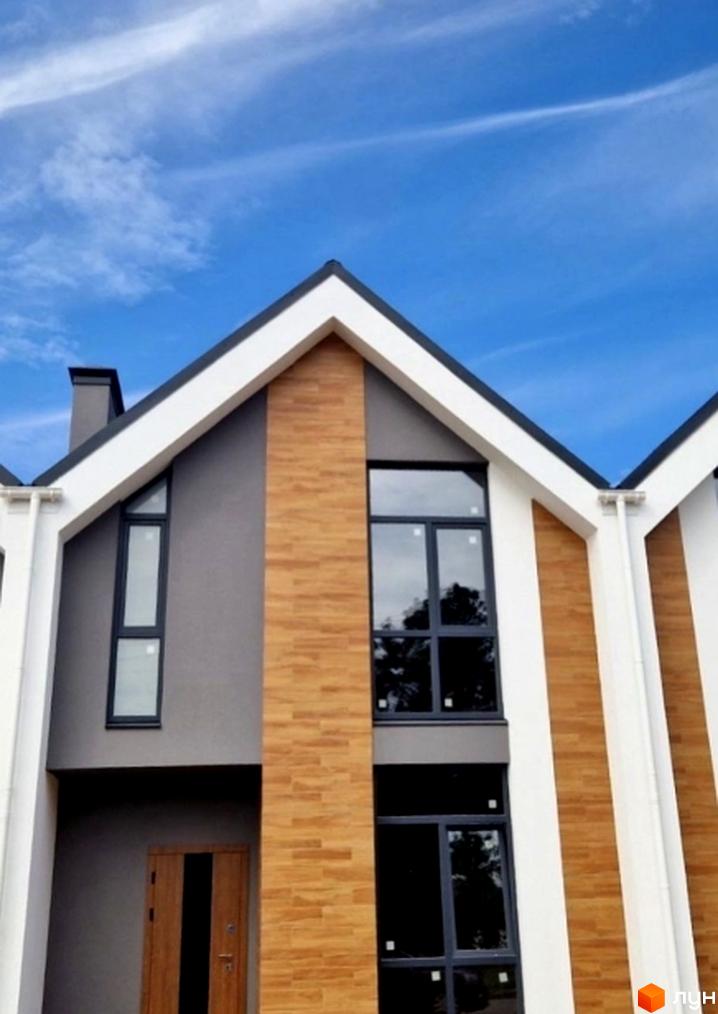 Таунхауси „На Водопровідній“: фасади будинків з великими вікнами та дерев'яними елементами під блакитним небом. Комплекс має сучасний вигляд.