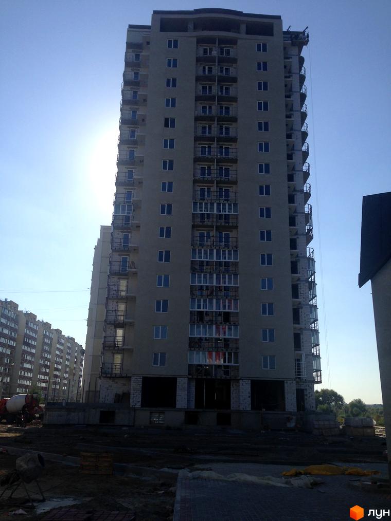 Житловий комплекс Маяк – висотна новобудова з численними балконами та вікнами. Будівельний майданчик з технікою та матеріалами.