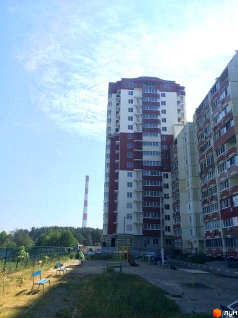 Житловий комплекс ЖБ Маяк: багатоповерхові будинки з червоно-білими фасадами та прибудинкова територія з зеленими насадженнями та лавками.