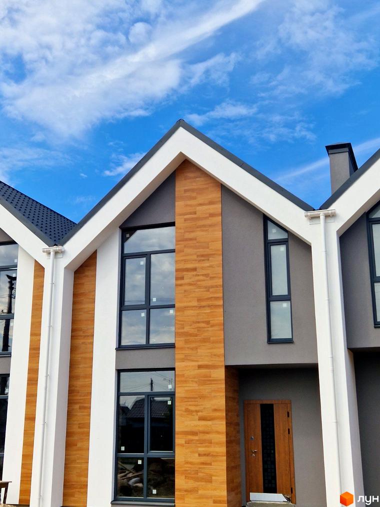 Зовнішній вигляд таунхаусів „На Водопровідній“ з великими вікнами та дерев'яними елементами фасаду під блакитним небом. Новобудова з сучасною архітектурою.