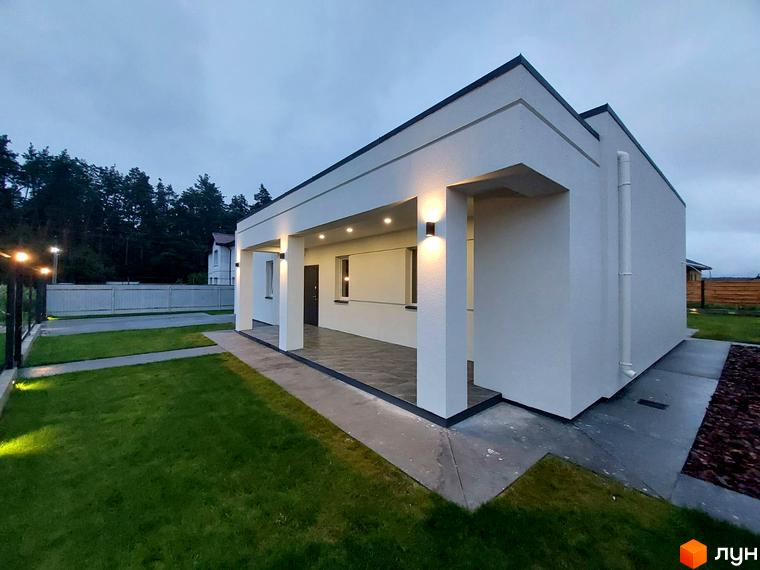 Сучасна одноповерхова новобудова КМ Лісне з терасою та підсвіткою. Навколо будинку доглянутий газон та доріжки.