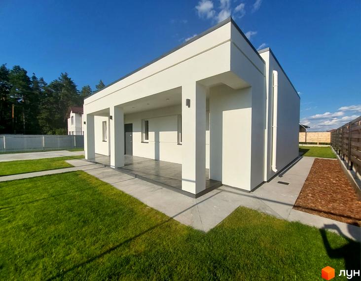 Котеджне містечко КМ Лісне: білий одноповерховий будинок з навісом та колонами, зелена галявина та бетонні доріжки.