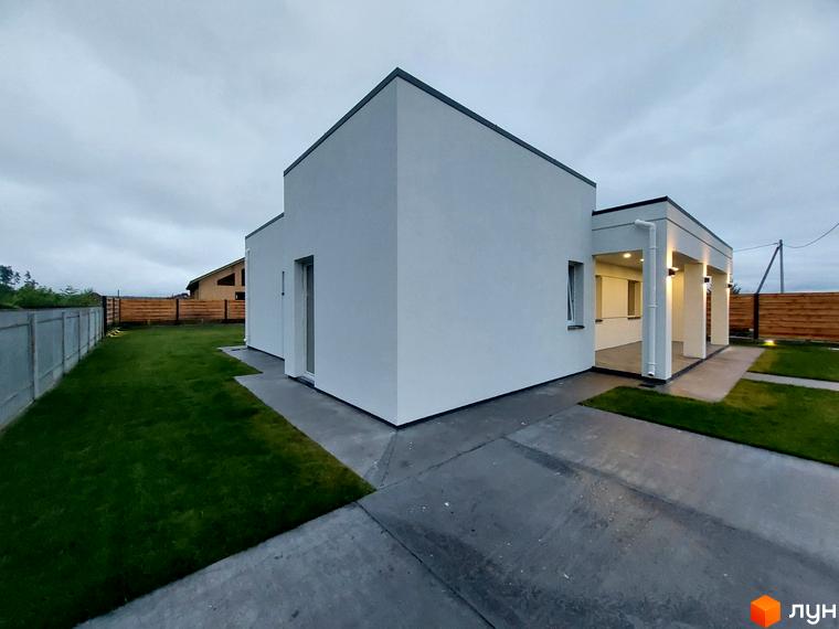 Котеджне містечко КМ Лісне: білий одноповерховий будинок з навісом та колонами, зелена галявина та бетонна доріжка.