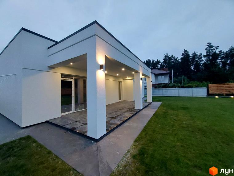 Котеджне містечко КМ Лісне: білий будинок з терасою та освітленням, зелена галявина та паркан.