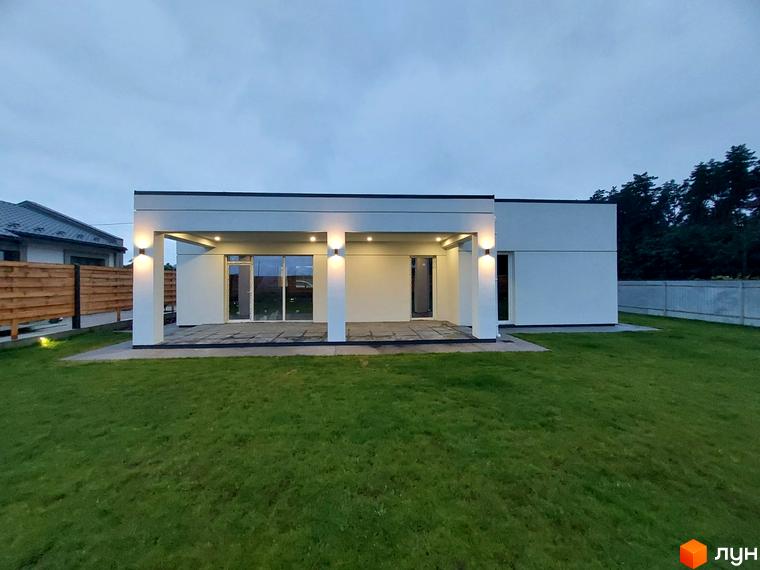 Котеджне містечко КМ Лісне: одноповерховий будинок з білою фасадною обробкою та навісом, освітленим двома ліхтарями. Навколо будинку доглянутий зелений газон.