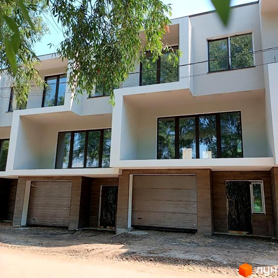 Таунхауси Laketown з фасадами білого кольору та великими вікнами. На першому поверсі розташовані гаражні ворота. Навколо видно зелені дерева та блакитне небо.