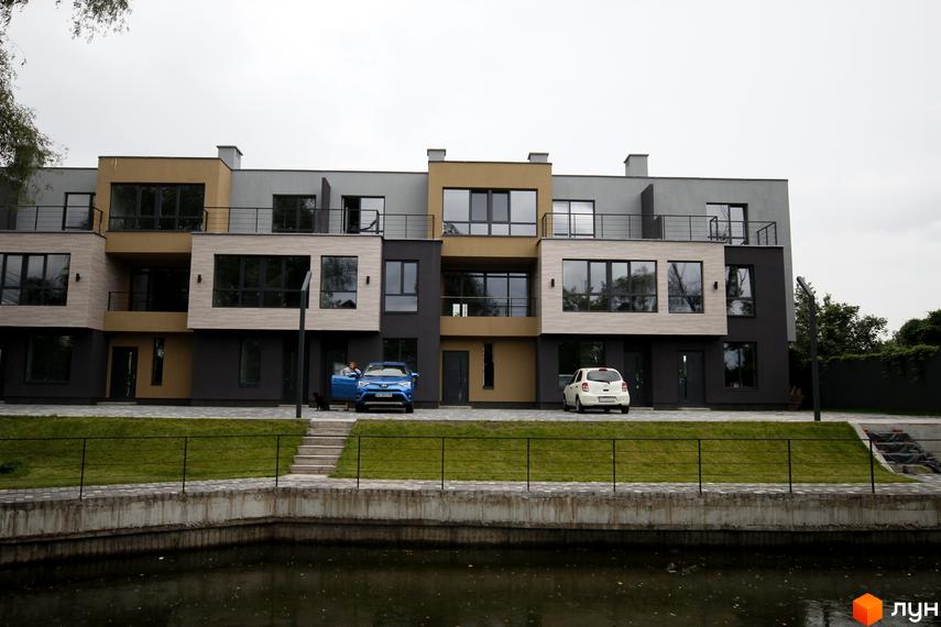 Зовнішній вигляд таунхаусів Rusaniv Gardens з фасадами у світлих тонах. Перед будинками газон та огороджена набережна.