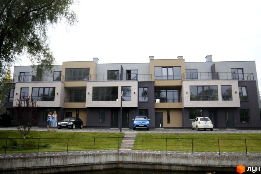 Триповерхові таунхауси Rusaniv Gardens з панорамними вікнами та парковкою. На території комплексу є доглянутий газон та водойма.