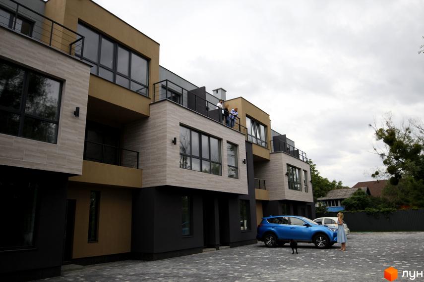 Зовнішній вигляд таунхаусів Rusaniv Gardens з великими вікнами та балконами. На прибудинковій території є парковка та зелені насадження.