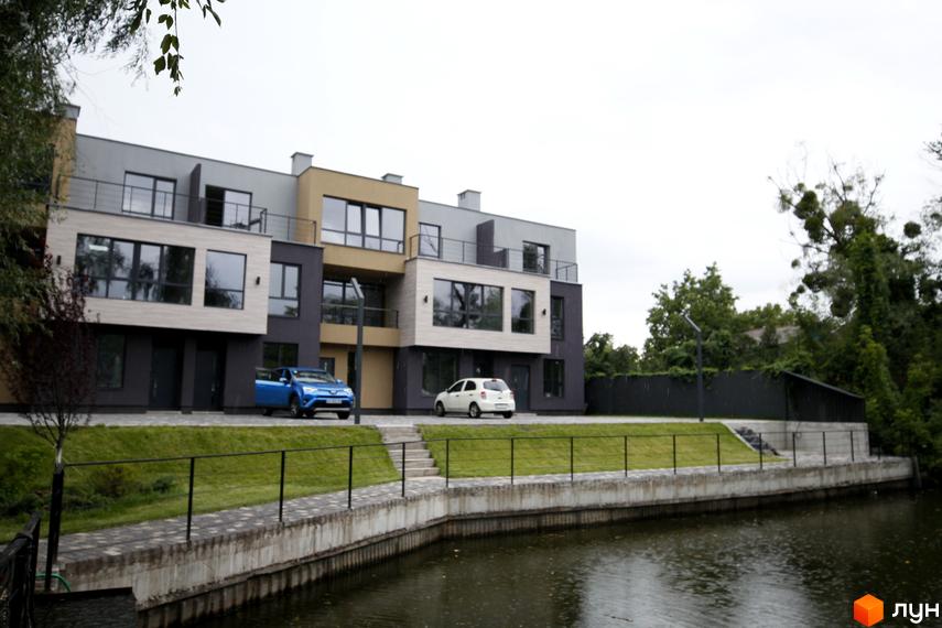 Вигляд таунхаусів Rusaniv Gardens з прибудинковою територією та водоймою. На подвір'ї припарковані автомобілі.