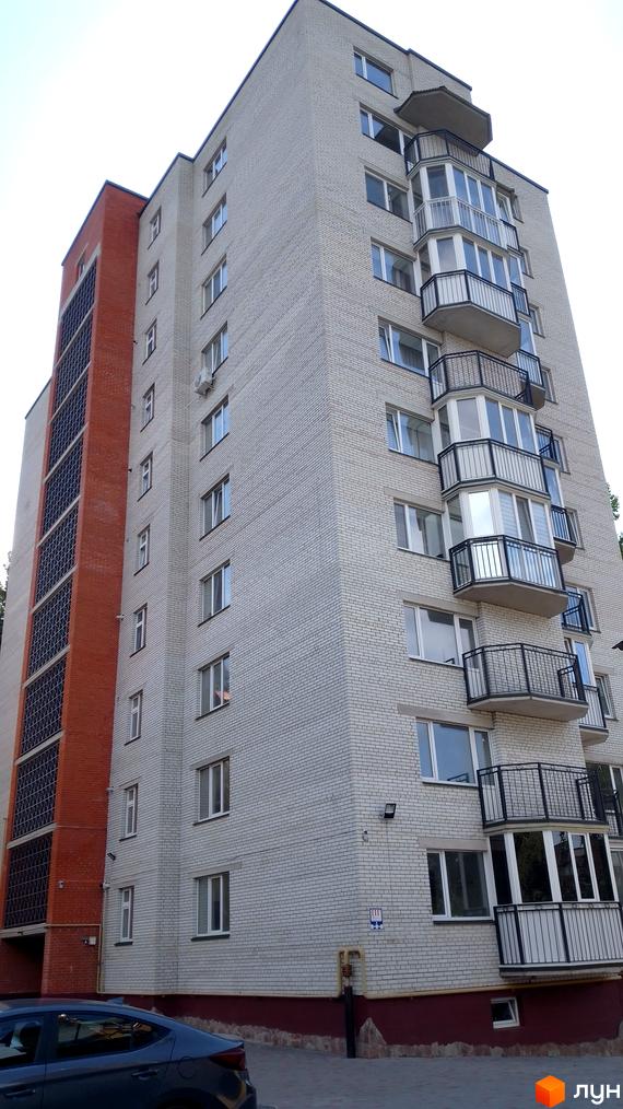 Будинок на вулиці Патріарха Любомира Гузара (Чалдаєва), 8а, з білої цегли та червоною вставкою з вікнами. Навколо будинку бруківка та зелені насадження.