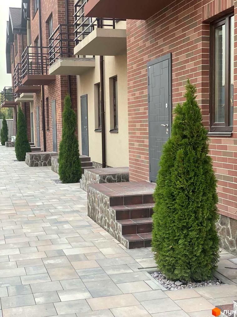 Зовнішній вигляд таунхаусів Modern House з цегляними фасадами, терасами та доглянутою прибудинковою територією з бруківкою та туями.