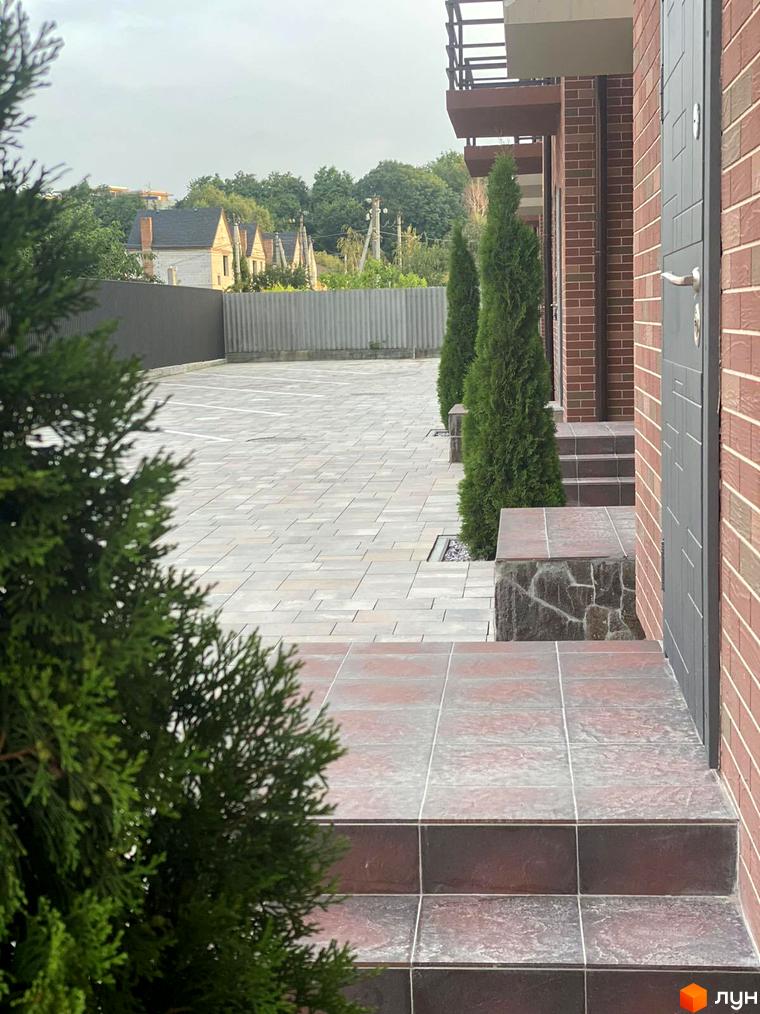 Зовнішній вигляд будинку Modern House з цегляним фасадом та сходами. На прибудинковій території бруківка та зелені насадження.