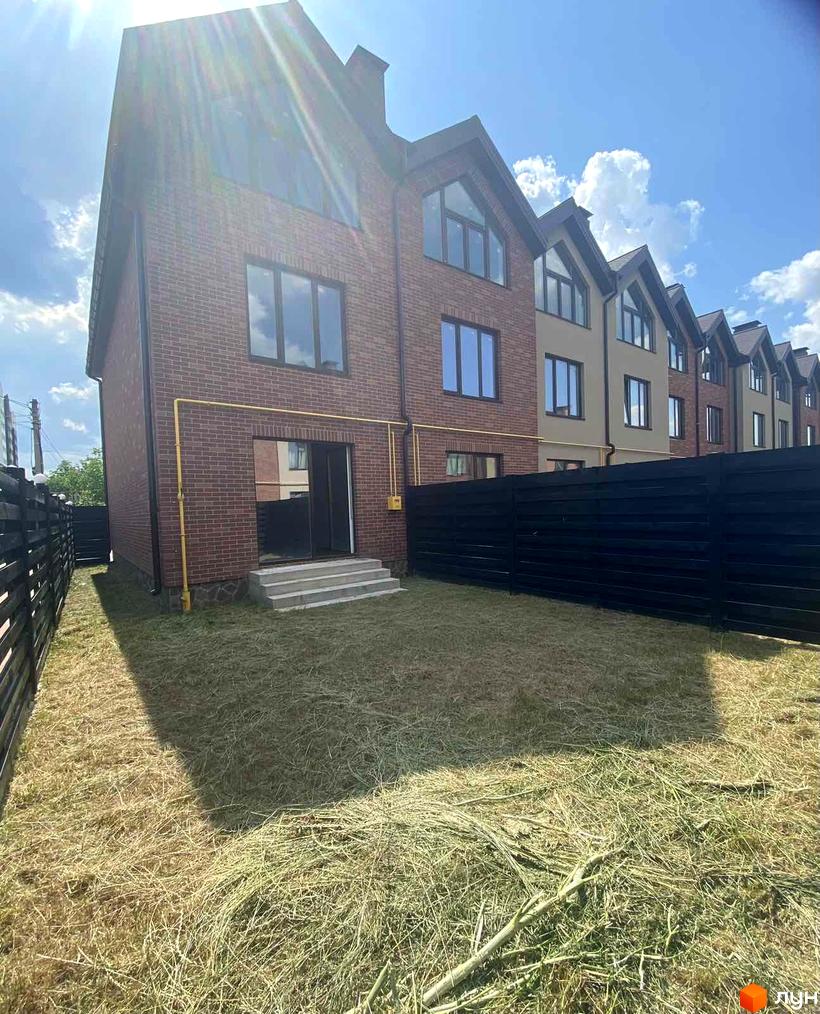 Цегляний будинок з панорамними вікнами на тлі блакитного неба. На передньому плані газон та чорний паркан, що огороджує територію.