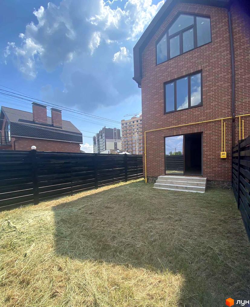 Цегляний будинок з панорамними вікнами та газовим обладнанням. На території будинку газон та чорний паркан.