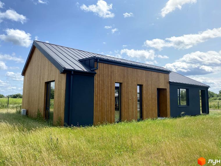 Котеджне містечко Mulberry Homes. Зовнішній вигляд будинку з дерев'яним фасадом та темним дахом на тлі зеленої трави та блакитного неба з хмарами.