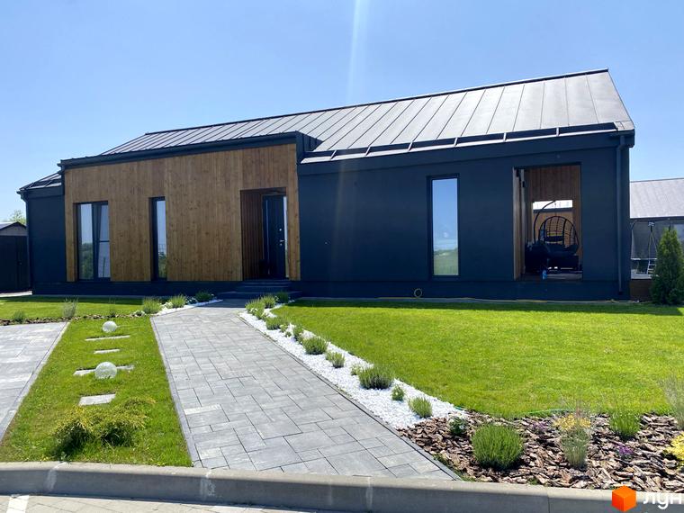 Зовнішній вигляд будинку в Котеджному містечку Mulberry Homes. На фото фасад будинку з темними стінами та дерев'яним оздобленням, доріжка з бруківки веде до входу, навколо газон.