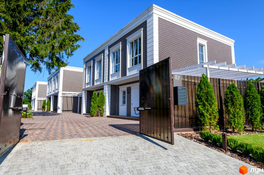 Таунхауси Feofaniya Home з цегляним фасадом та білими елементами, перед якими розташована брукована територія та зелені насадження.