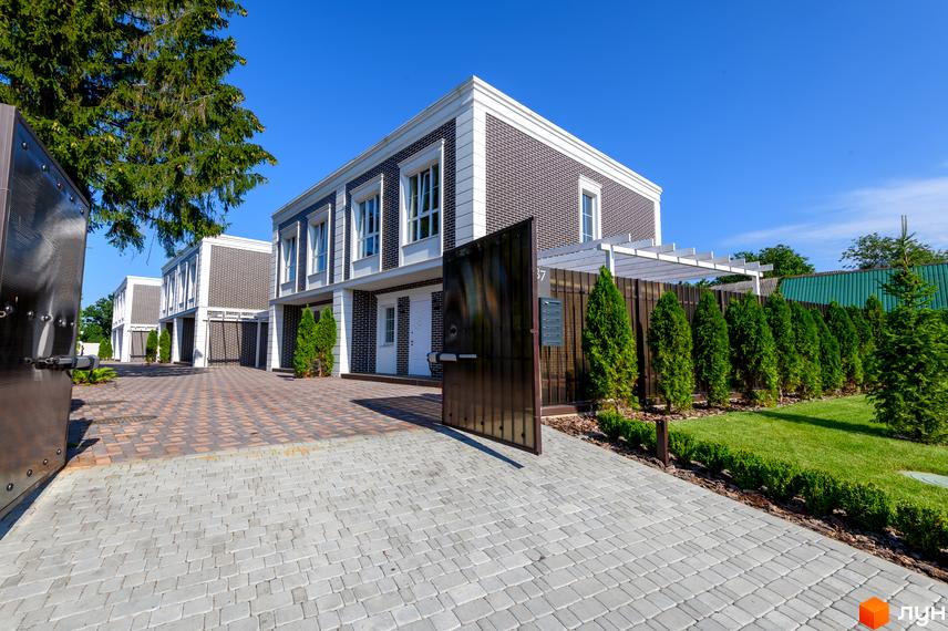 Таунхауси Feofaniya Home з цегляним фасадом та білою обробкою, розташовані на брукованій території з акуратно підстриженими туями та газоном.
