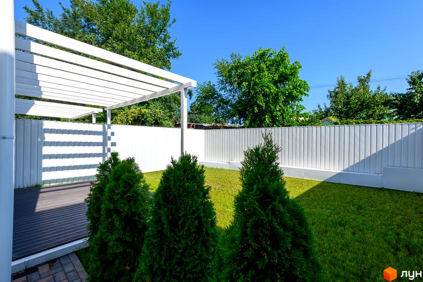 Таунхауси Feofaniya Home: білий паркан, зелений газон та дерева під блакитним небом. Тераса з дерев'яним покриттям та навісом.