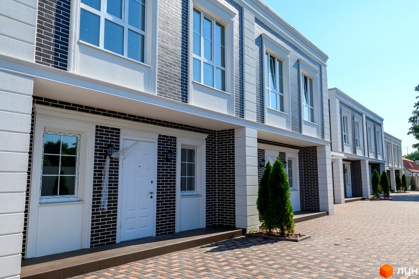 Таунхауси Feofaniya Home з цегляним фасадом та білими елементами, перед будинками розташована бруківка та зелені насадження.