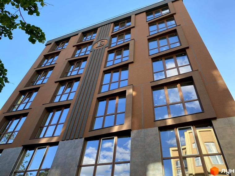 Фасад житлового комплексу Elegant з коричневими панелями та великими вікнами, що відбивають небо та хмари. Будинок має геометричний дизайн з вертикальними елементами.