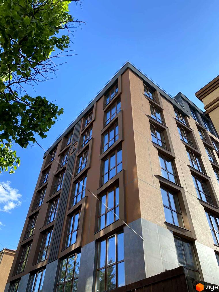 Зовнішній вигляд будинку житлового комплексу Elegant. Фасад оздоблений коричневою штукатуркою та сірою плиткою, великі вікна з темними рамами.