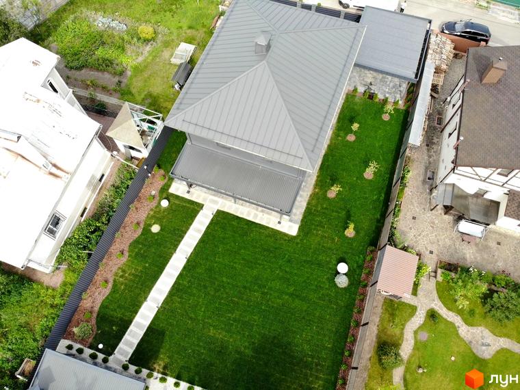 Будинок Котеджного містечка Kulbaba Petropavlivka з сірим дахом та фасадами. На території доглянутий зелений газон з доріжкою та молодими деревами.