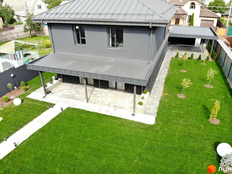 Двоповерховий сірий будинок з критою терасою. На території Котеджного містечка Kulbaba Petropavlivka доглянутий газон та доріжки.