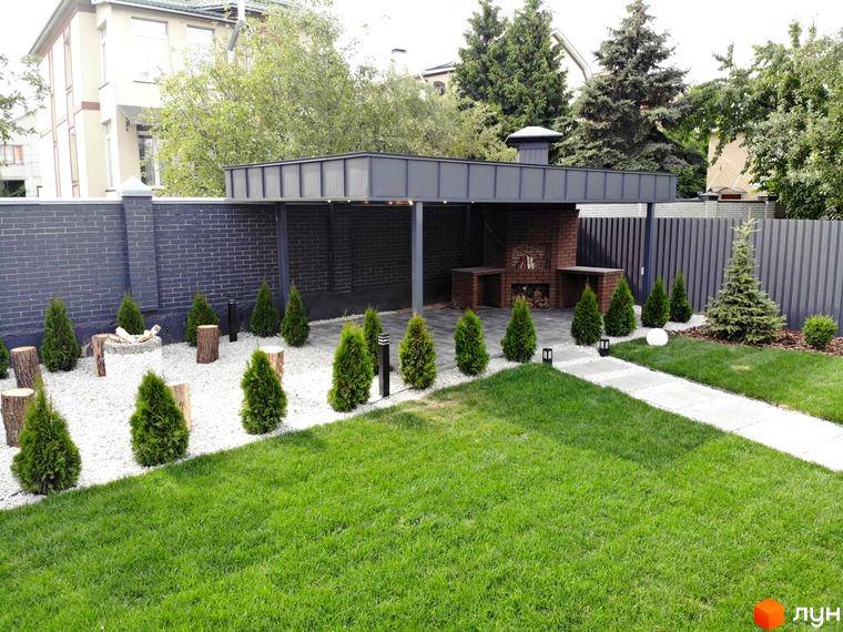 Вид на будинок Котеджного містечка Kulbaba Petropavlivka та облаштовану прибудинкову територію з зоною барбекю, газоном і декоративними деревами.