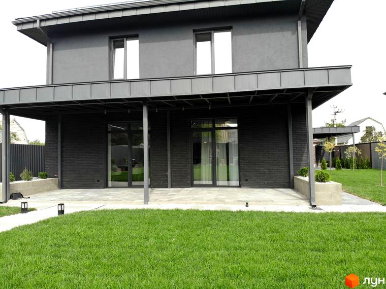 Двоповерховий будинок Котеджного містечка Kulbaba Petropavlivka з темним фасадом та панорамними вікнами, перед яким розташований доглянутий газон.