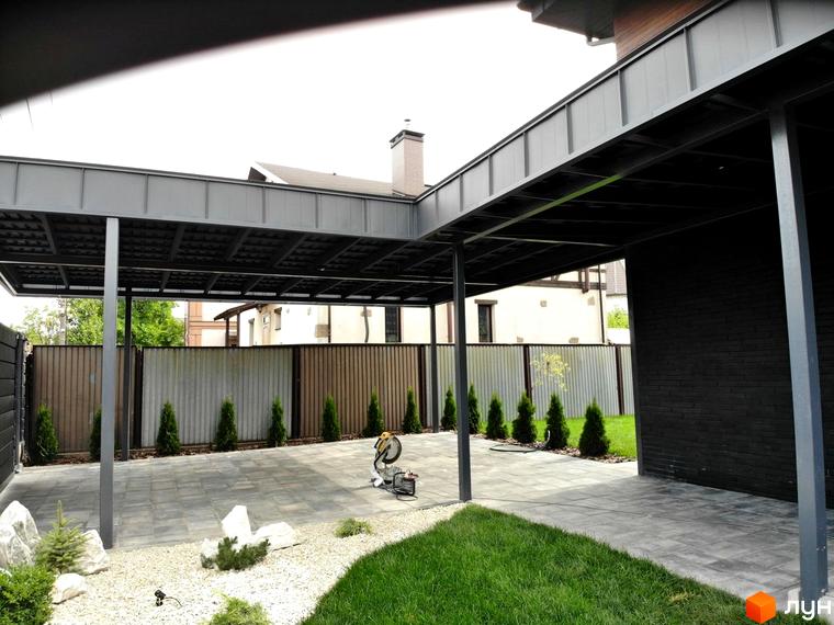 Котеджне містечко Kulbaba Petropavlivka: фрагмент будинку з темною цеглою, сірий навіс для авто та подвір'я з бруківкою.