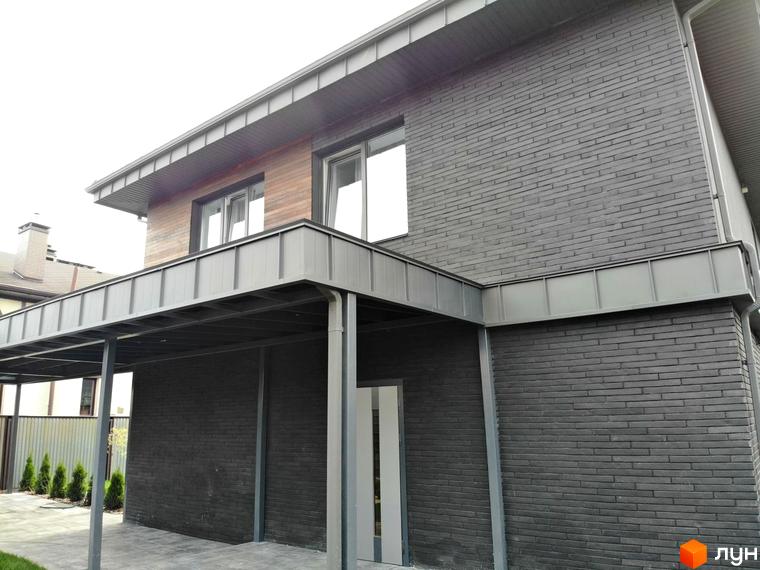 Котеджне містечко Kulbaba Petropavlivka: фасад будинку з темно-сірої цегли та дерев'яних панелей, з навісом для автомобіля та брукованим подвір'ям.