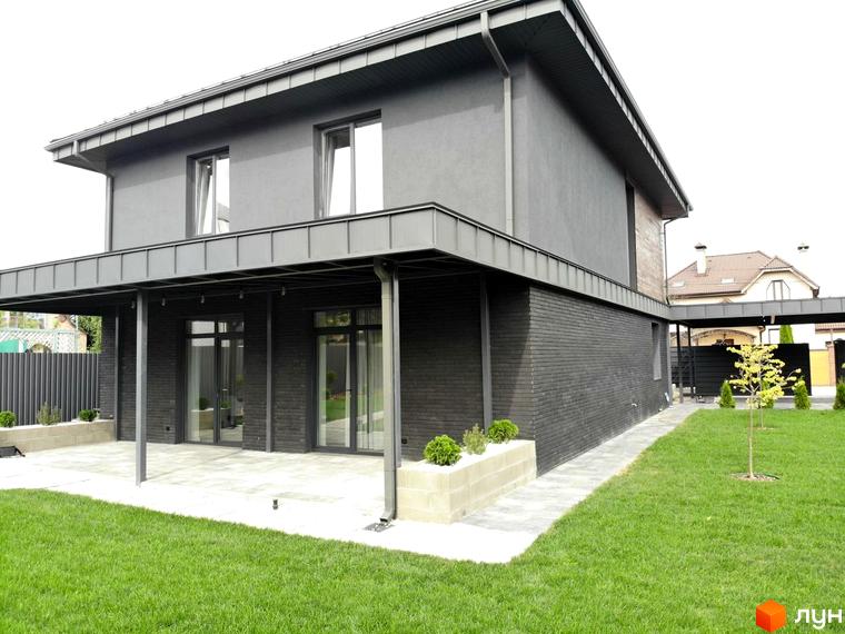 Двоповерховий будинок Котеджного містечка Kulbaba Petropavlivka з темно-сірим фасадом та великими вікнами. Перед будинком вимощена тераса та зелений газон.