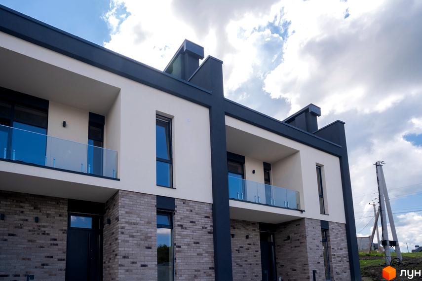 Зображення фасаду Котеджного містечка Квадрат TOWN з балконами та цегляною кладкою. Навколо новобудови облаштована прибудинкова територія.