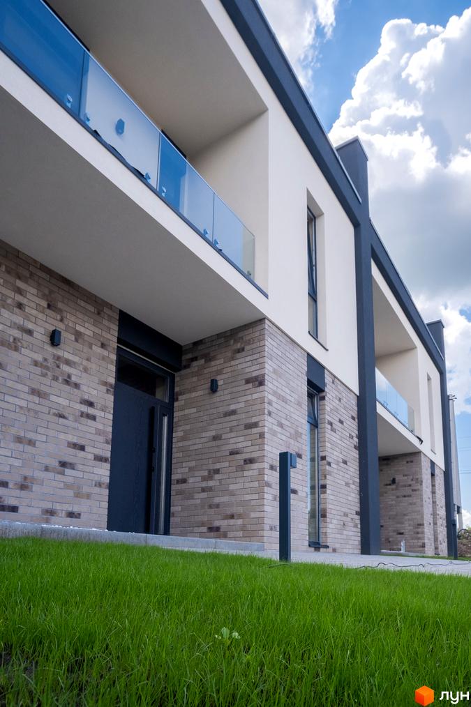 Зображення фасаду та балконів Котеджного містечка Квадрат TOWN з цегляною кладкою та газоном перед будинком.