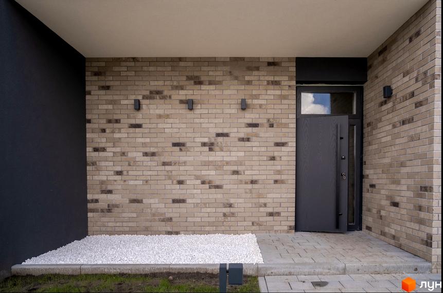 Зовнішній вигляд будинку в Котеджному містечку Квадрат TOWN з оздобленням стін цеглою. Перед будинком біла кам'яна крихта та плитка.