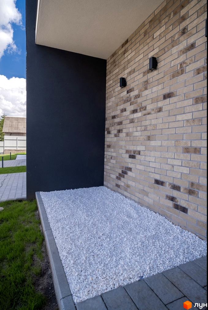 Фасад будинку Котеджного містечка Квадрат TOWN з комбінованою обробкою цеглою та темною штукатуркою. Прибудинкова територія з білою галькою та газоном.